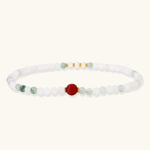 Three layered white beaded bracelets with carved orange agate lotus centerpiece and freshwater pearls on cream background.