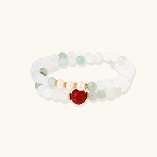 Three layered white beaded bracelets with carved orange agate lotus centerpiece and freshwater pearls on cream background.